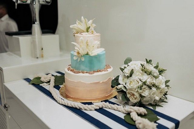 Three-tier wedding cake with white flowers on a table aboard a catamaran