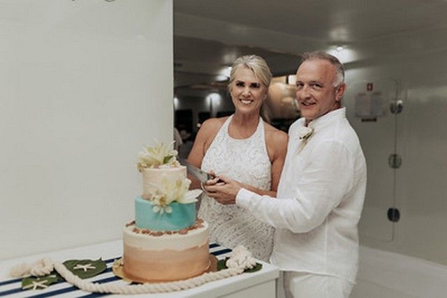 Newlyweds cutting a tiered wedding cake aboard a catamaran
