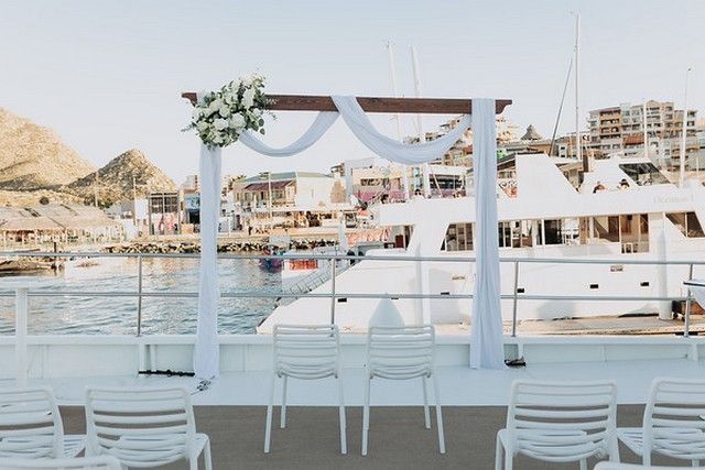 Wedding ceremony arch and white chairs set up on the deck of a catamaran in the marina